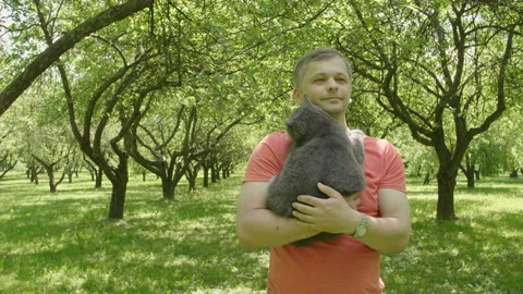 Happy smiling handsome man Stroking a Cat and walks through green trees alley. 库存影片 110779899