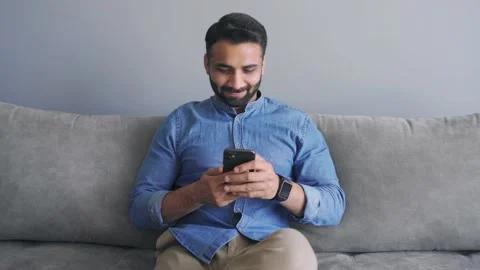 Happy smiling millennial indian man in causal jeans shirt using mobile app Stock Footage 157482934