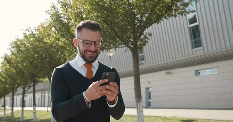 Happy Smiling Office Manager walking in the City while Using his Smartphone Stock Footage 124658968
