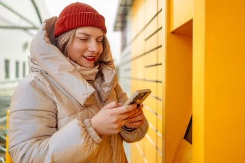 Happy smiling woman client with box at outdoor automated parcel machine choosing Stock Photos