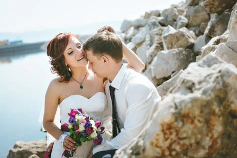 Happy smiling young bride and groom, walking on the rocks, beautiful sky, water Stock Photos