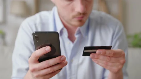 Happy smiling young man sit on sofa buying online use cellphone and credit card Stock Footage 169017486