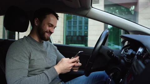 Happy smiling young man sitting in car and typing online message on cell phone Video stock 140220161