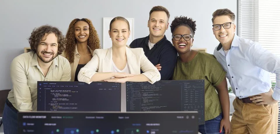 Happy software developers team portrait in startup office behind coding monitors Stock Photos