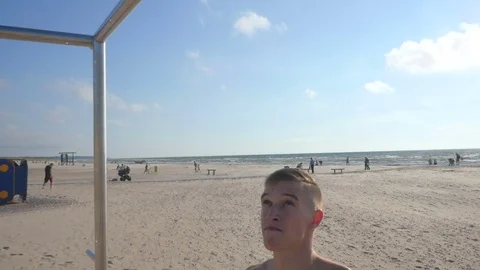 Happy strong bodybuilder at the beach doing pull ups, bar view Video stock 84041811