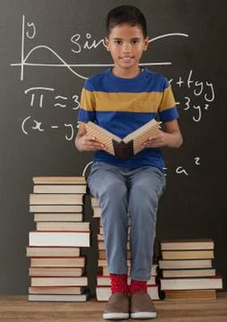 Happy student boy on a table reading against grey blackboard with education and 写真素材