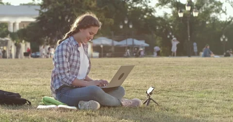 Happy student does homework on laptop sitting on grass Stockbeeldmateriaal 154577232