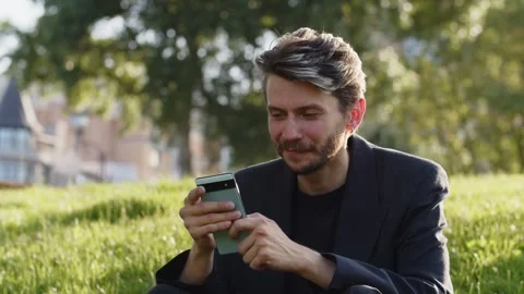 Happy student man using his new phone gadget in nature. Positive guy reading Stock Footage 251715547