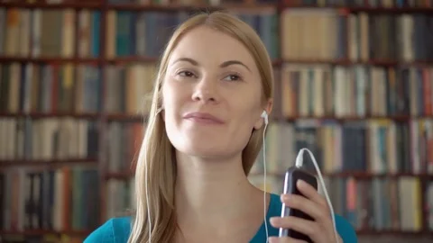Happy student standing in library using smartphone listening music on smartphone Stock Footage 75409829