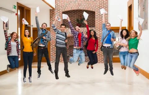 Happy students jumping for joy holding exam results in a hallway Stock Photos
