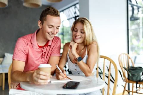 Happy students sitting in cafe table of university and doing homework or writing Stock Photos