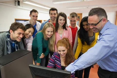 Happy students standing at computer with their lecturer in the computer room Photos