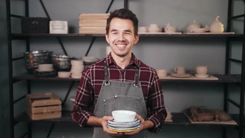 Happy successful potter in workshop studio posing and smiling behind shelves 스톡 동영상 143272294