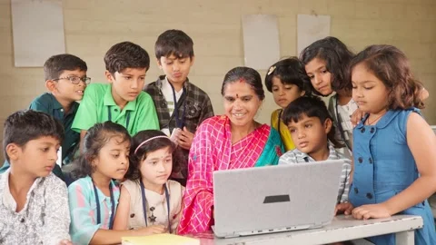 Happy teacher teaching from laptop to elementary students around at classroom - Stock Footage 200828144