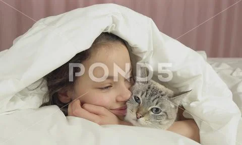 Happy teen girl kisses and talks with Thai cat in bed Stock Photos