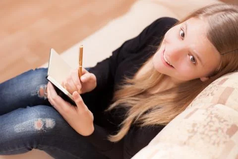Happy teen writing to the diary sitting on the sofa in the living room Stock Photos