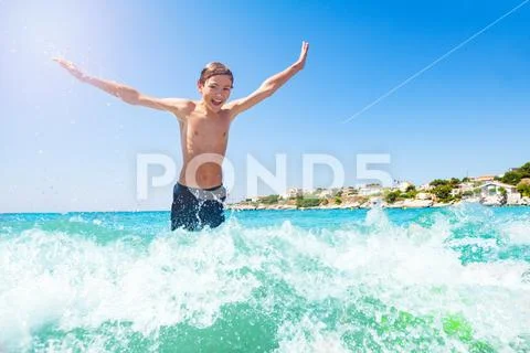 Happy teenage boy jumping in shallow water wave Stock Photos
