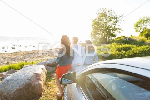 Happy teenage girls or women near car at seaside Stock Photos