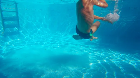 Happy ten year old boy having fun in a swimming pool, diving underwater and Stock Footage 344687374