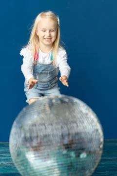 Happy toddler blonde girl havig fun while rolling giant disco ball on the floor Stock Photos