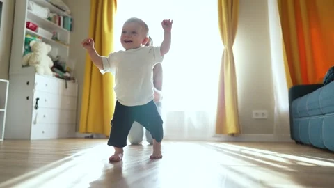 Happy toddler takes first steps barefoot. Mother encourages toddler with smiles Stock Footage 346306872