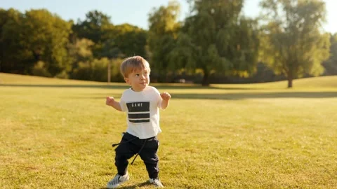 Happy toddler taking first steps on grassy meadow in park, Stock Footage 310439093