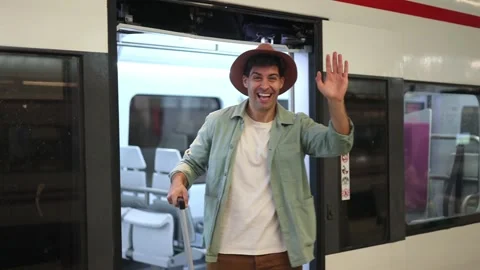 Happy traveler waving to camera while getting off train with suitcase at va.. Stock Footage 298562962
