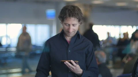 Happy traveling man sms texting using app on smart phone in airport Stock Footage