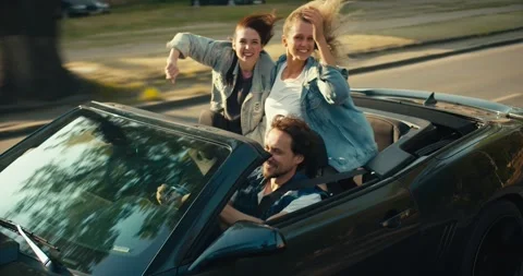 A happy trio: a guy and two girls are riding in a gray convertible. A blonde Stock Footage 245827028