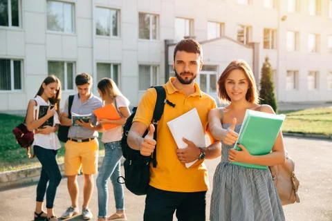Happy two young students with note-books and backpacks smiling and showing th Stock Photos