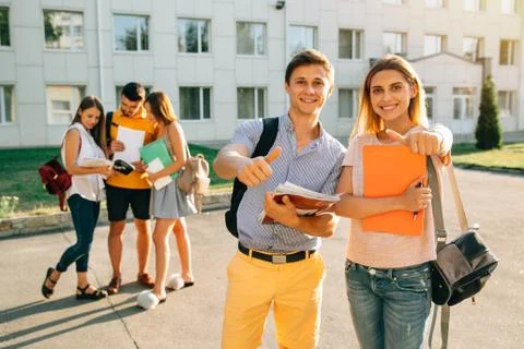 Happy two young students with note-books and backpacks smiling and showing th Stock Photos