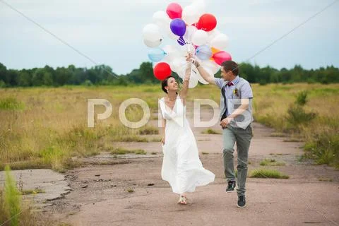 Happy Wedding Couple Runs Holding In Hands Colorful Latex Balloons. Happy People