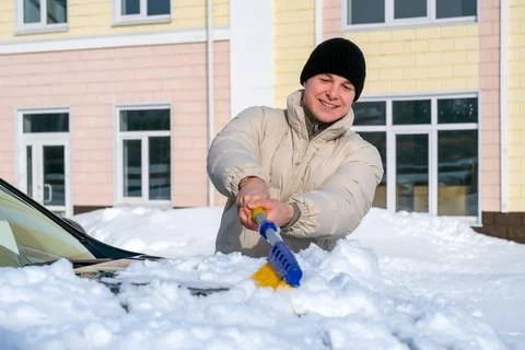 Happy winter routine concept smiling young driver cleaning snow from car ho.. Stock Photos
