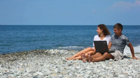 Happy woman and man with notebook sitting in rocky beach Stock Footage
