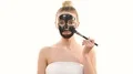 The happy woman applying a skin care black mask on the white background 4k or 4k+ Resolution