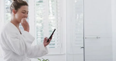 Happy woman brushing teeth using smartphone in bathroom, slow motion Stock Footage 340068469