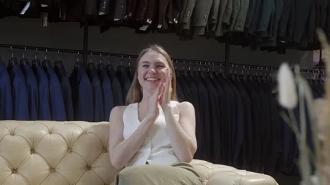 Happy woman clapping while sitting on sofa in fashion store Stock Footage 303459495