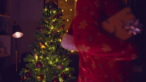 Happy Woman Dancing While Carrying a Wrapped Christmas Gift Beside a Decorated T Stock Footage 338193624