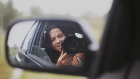 Happy woman doing selfie with camera in a car mirror and smiling in moving car Stock Footage 80340321