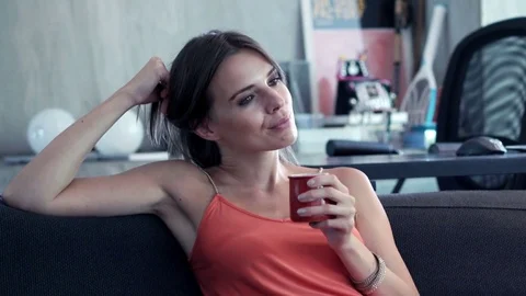 Happy woman drinking beverage while relaxing on sofa at home Stock Footage 72349374