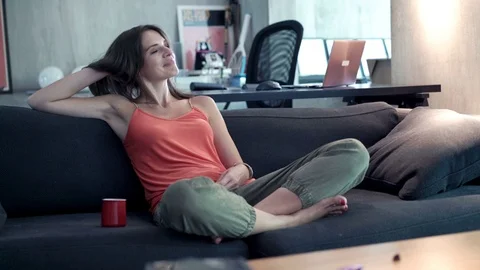 Happy woman drinking beverage while relaxing on sofa at home, 4K Stock Footage 72441853