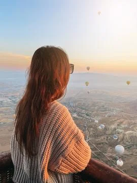 Happy woman during sunrise watching hot air balloons show from a basket in the Stock Photos