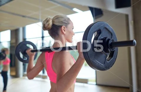Happy woman flexing muscles with barbell in gym Stock-Fotos