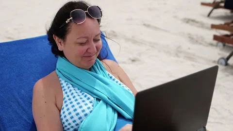 Happy woman gesturing while working on laptop at beach Stock Footage 249764745