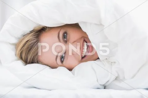 Happy woman hiding under the duvet Stock Photos