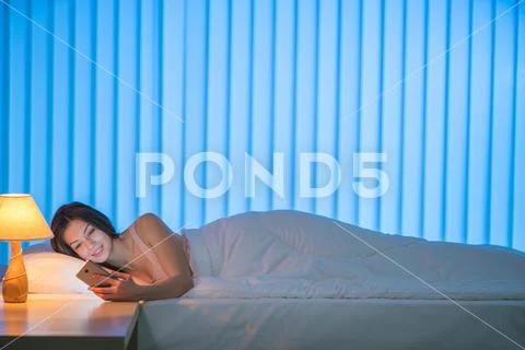 The happy woman lay on the bed and phone. Evening night time Stock Photos