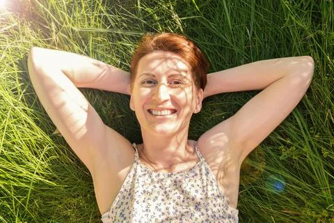 Happy woman lies in the grass in the rays of the setting sun and smiles Stock Photos