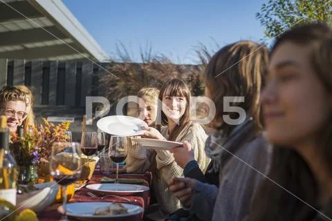 Happy woman passing plates to friends during garden party Stock Photos