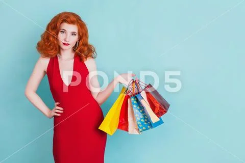 Happy woman in red dress with shopping bags on a blue background. Stock Photos