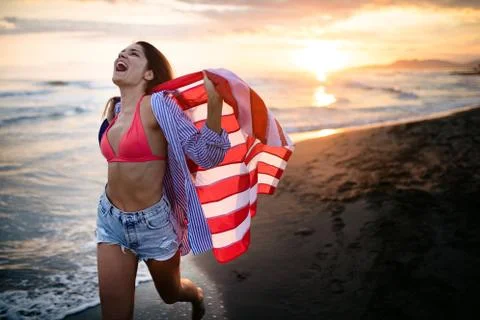 Happy woman running on beach while celebrateing independence day and enjoying Stock Photos
